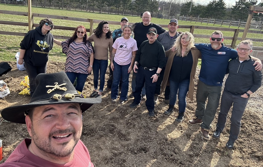 Volunteers, veterans, and friends gather at the ranch on a bright spring day.